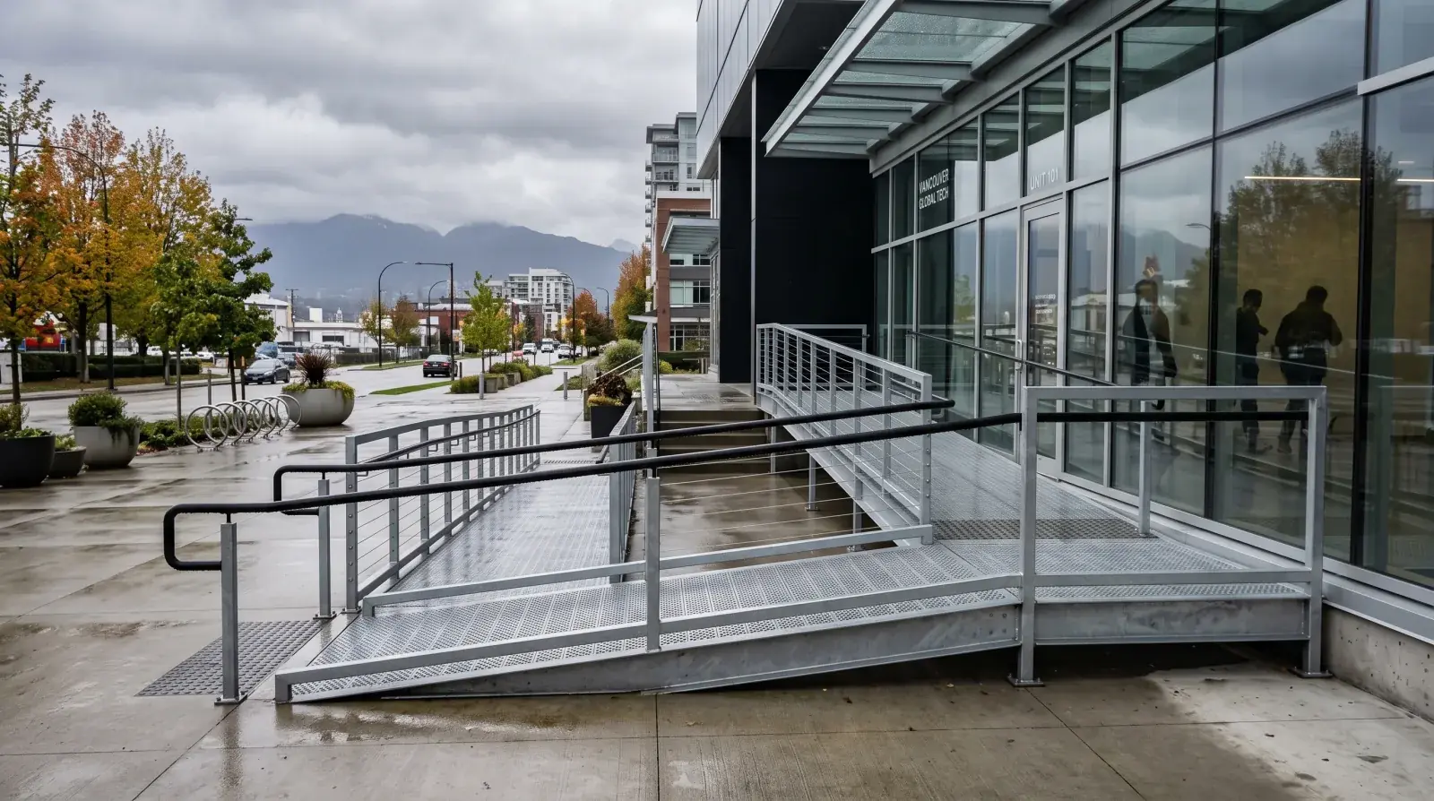 Modern galvanized steel accessibility ramp with switchback landing and handrails on both sides at a commercial building in Vancouver