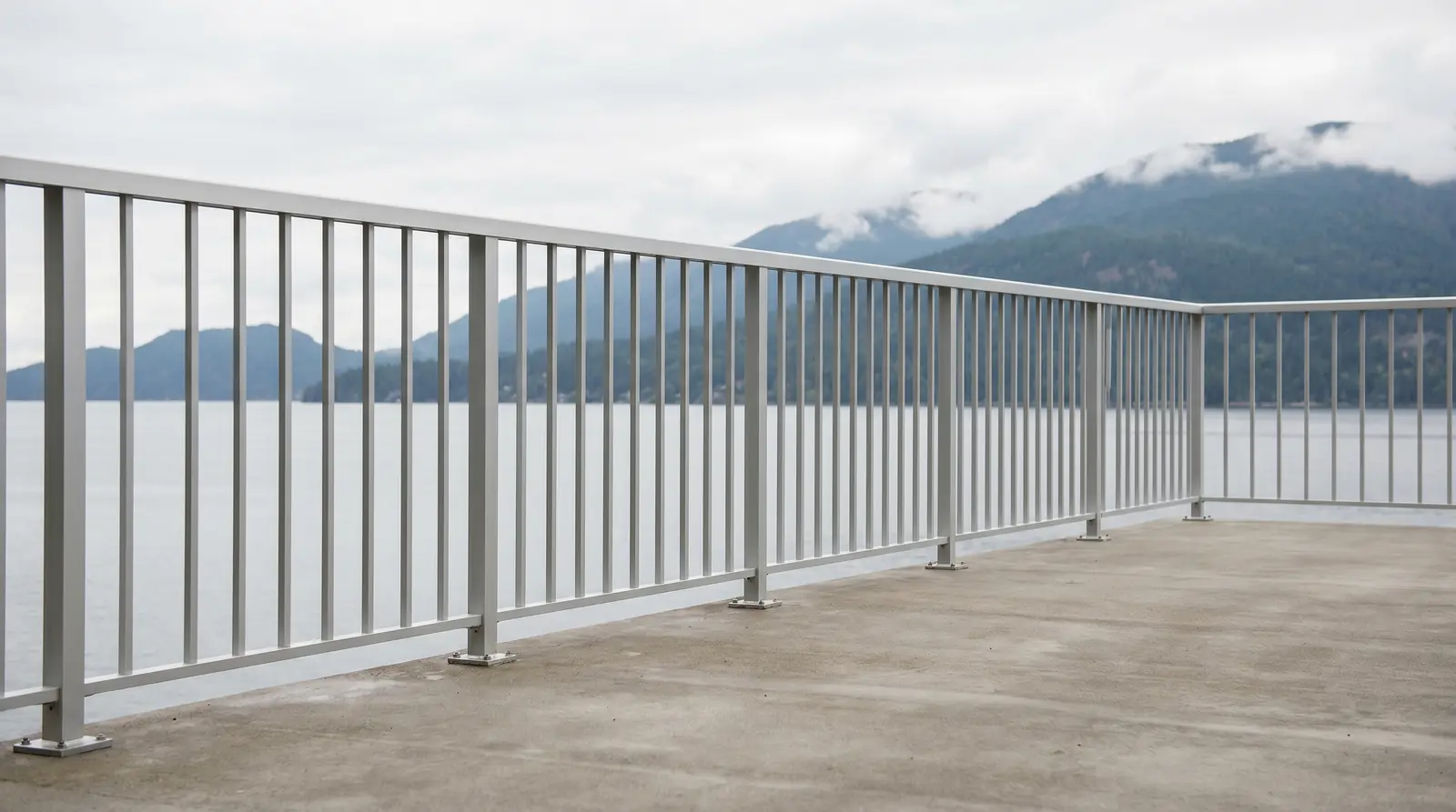 Modern satin-anodized aluminum guard railing with thin vertical pickets on a contemporary West Vancouver concrete deck overlooking Burrard Inlet, North Shore mountains in soft overcast Pacific Northwest light