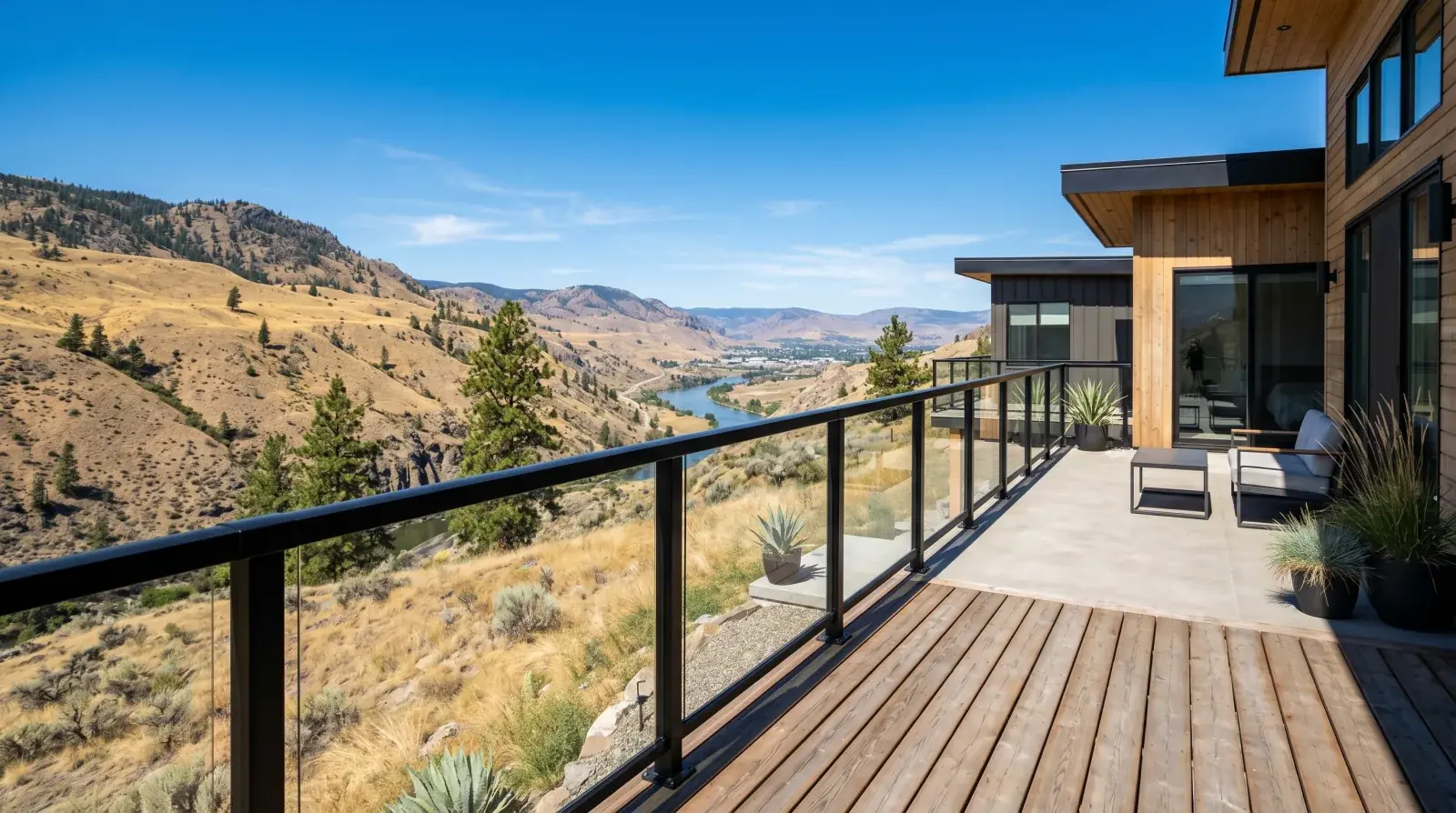 Matte black steel and glass deck guardrail on a Kamloops hillside home overlooking the dry Thompson River valley under strong summer sun