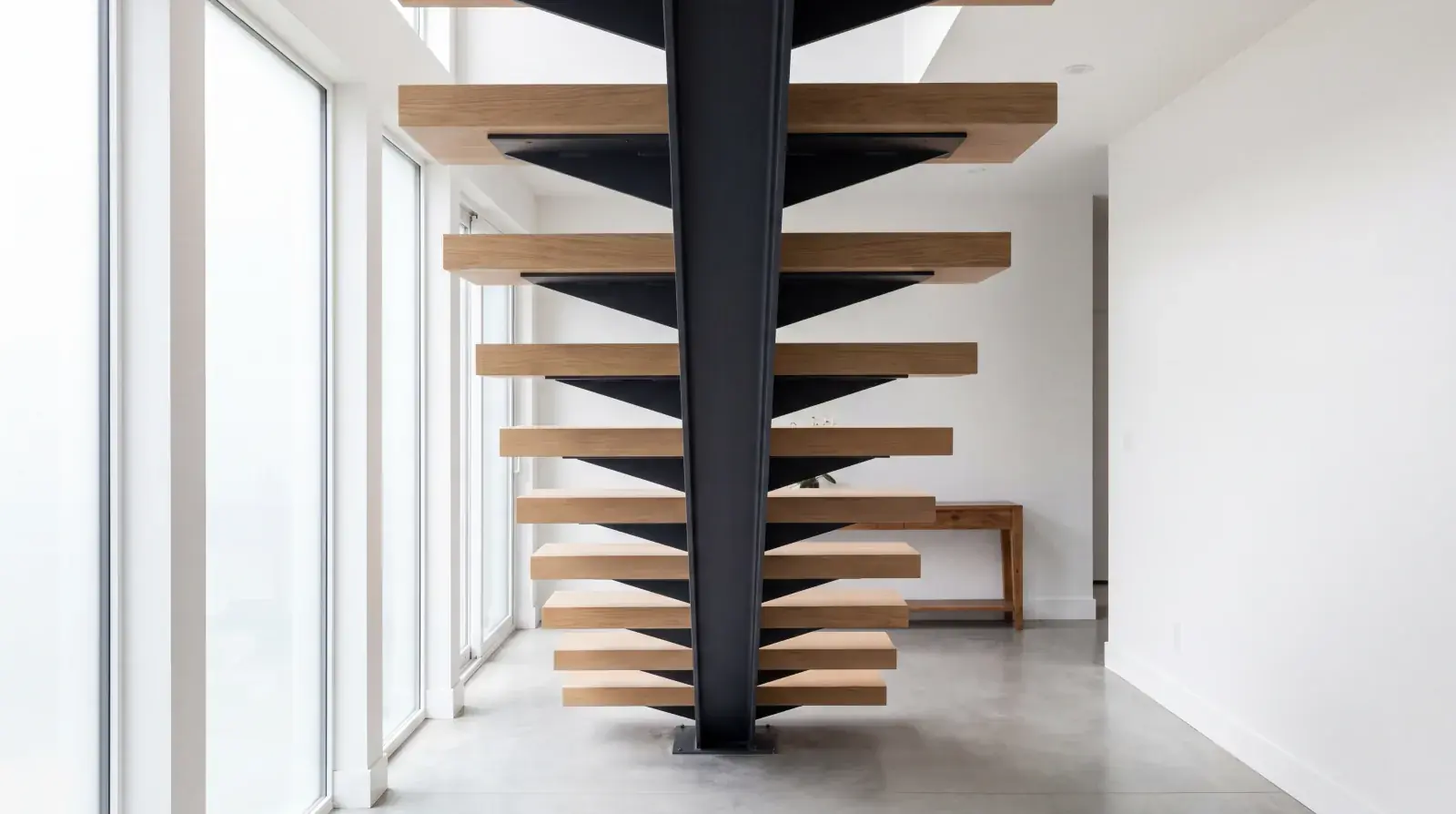 Code-compliant mono stringer staircase, single central blackened steel spine with cantilevered hardwood treads, being installed in a Metro Vancouver home