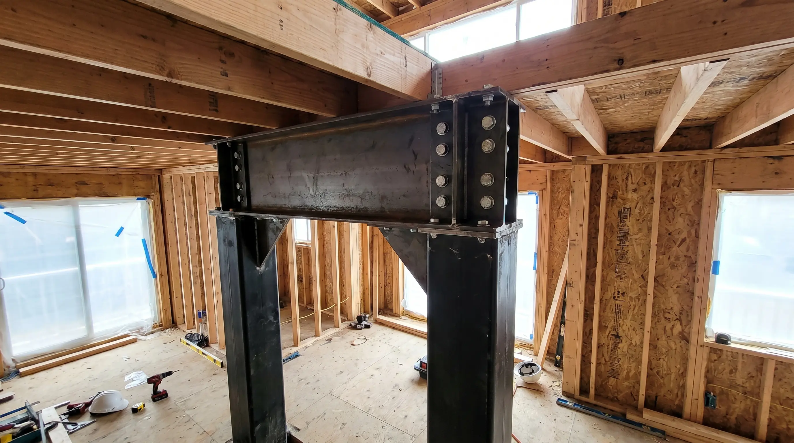 Residential structural steel installation, wide-flange steel beam on HSS columns with bolted plate connections inside a wood-framed Vancouver home renovation
