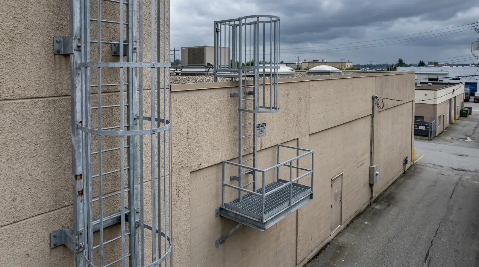 Galvanized steel roof-access ladder with safety cage and platform on a Burnaby commercial building