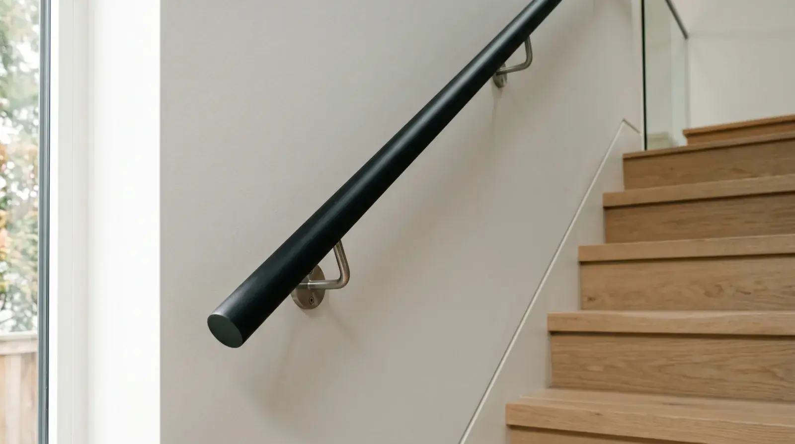 Modern matte-black round steel handrail on stainless standoff brackets along a Vancouver home stair wall