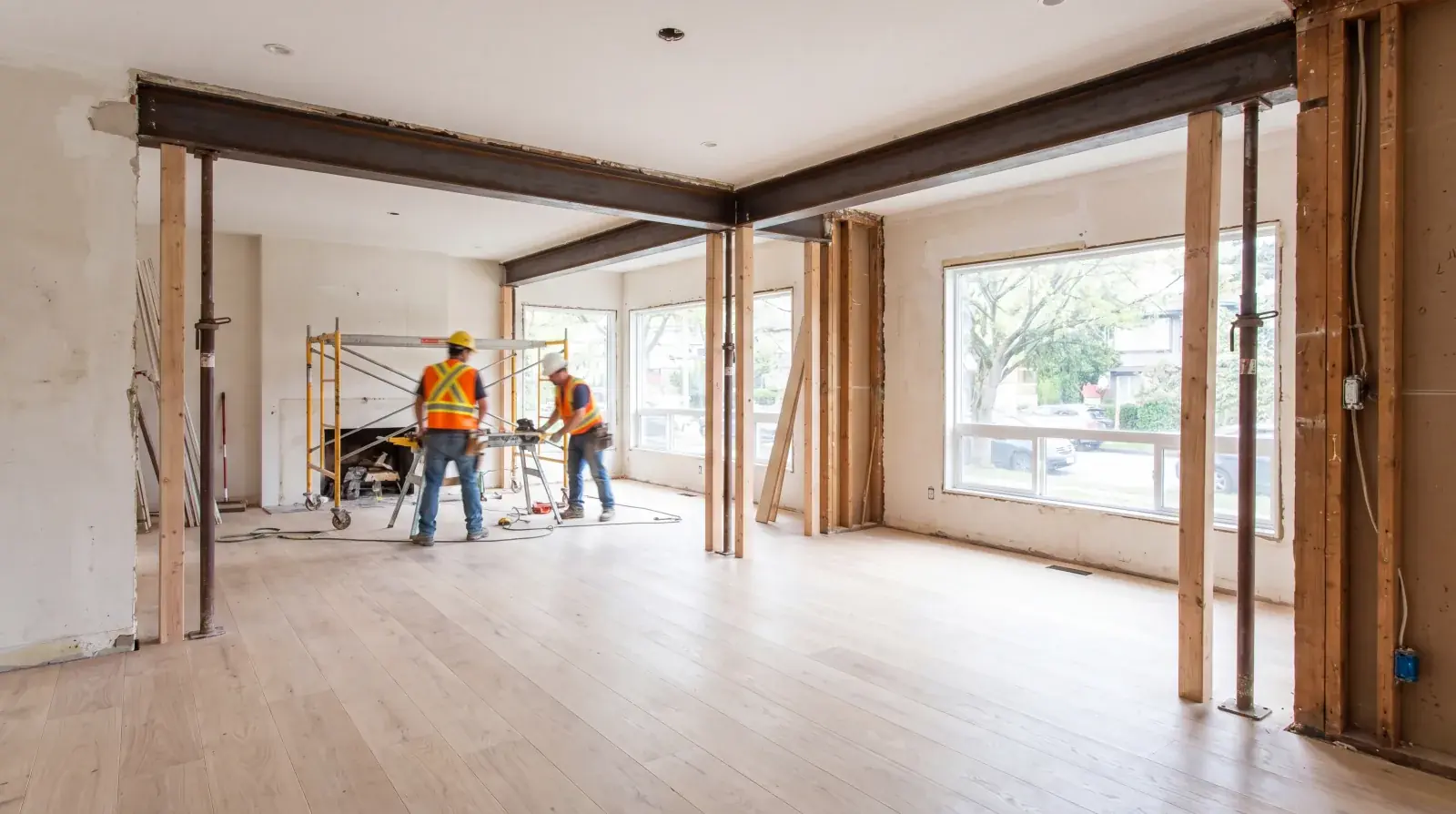 Structural steel beams set into a wood-framed Metro Vancouver residence during installation, with tagged W-shape members spanning over a poured rebar slab below