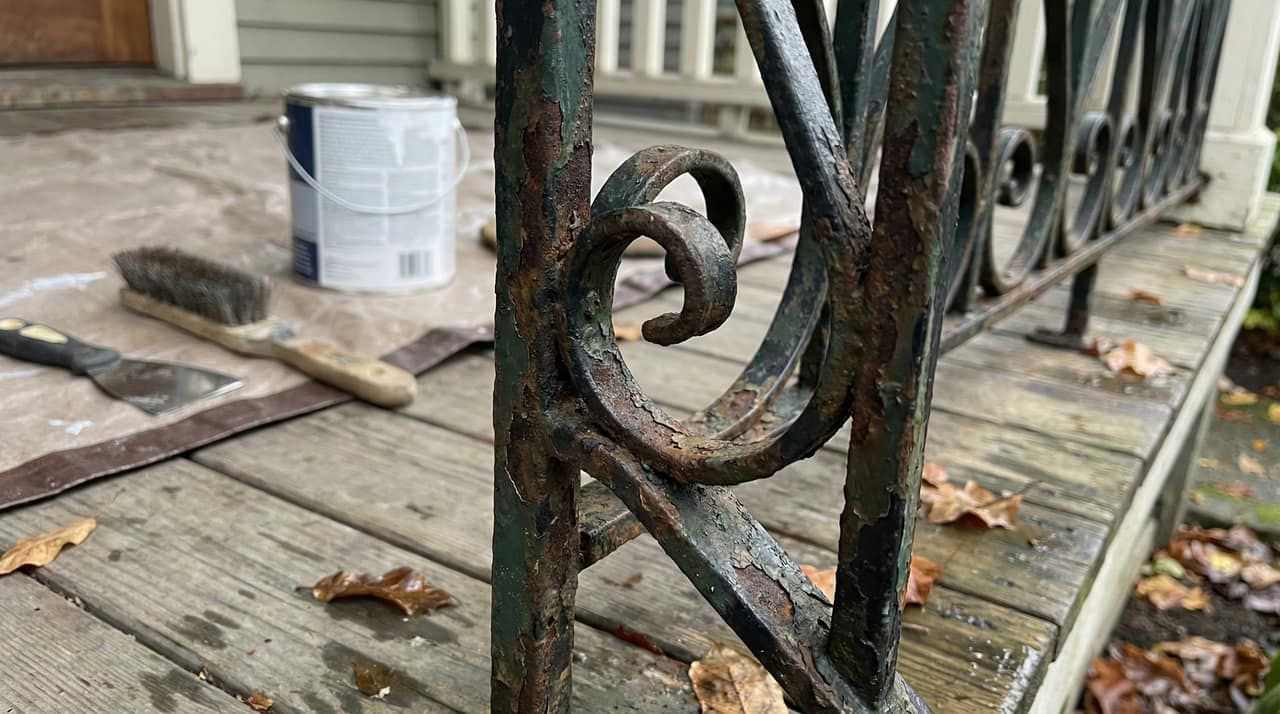Rusted heritage wrought iron railing with peeling paint and a hand-forged scroll detail being prepared for restoration on a West End character home porch