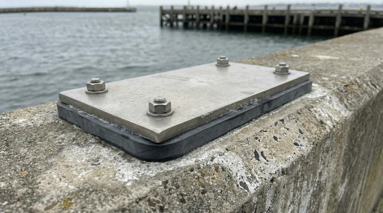 Close-up of a 316L stainless steel base plate mount on a concrete seawall with neoprene isolation gasket