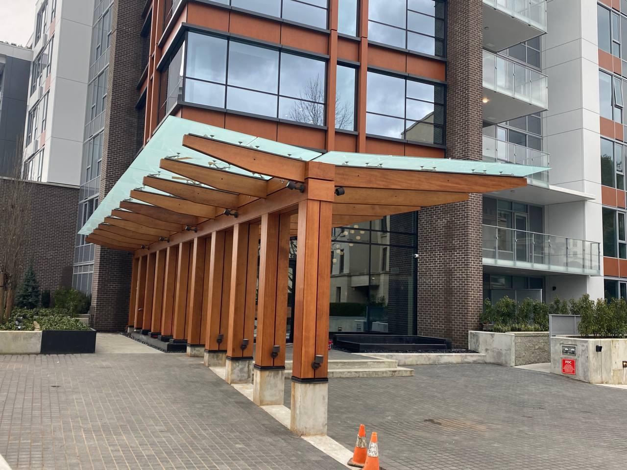 Structural steel and glulam timber porte-cochère with engineered glass roof on a mixed-use residential tower in Burnaby
