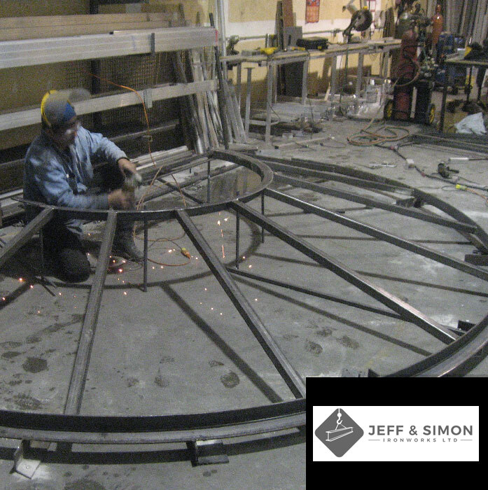 Welder fabricating a large circular steel canopy frame in the Jeff and Simon workshop