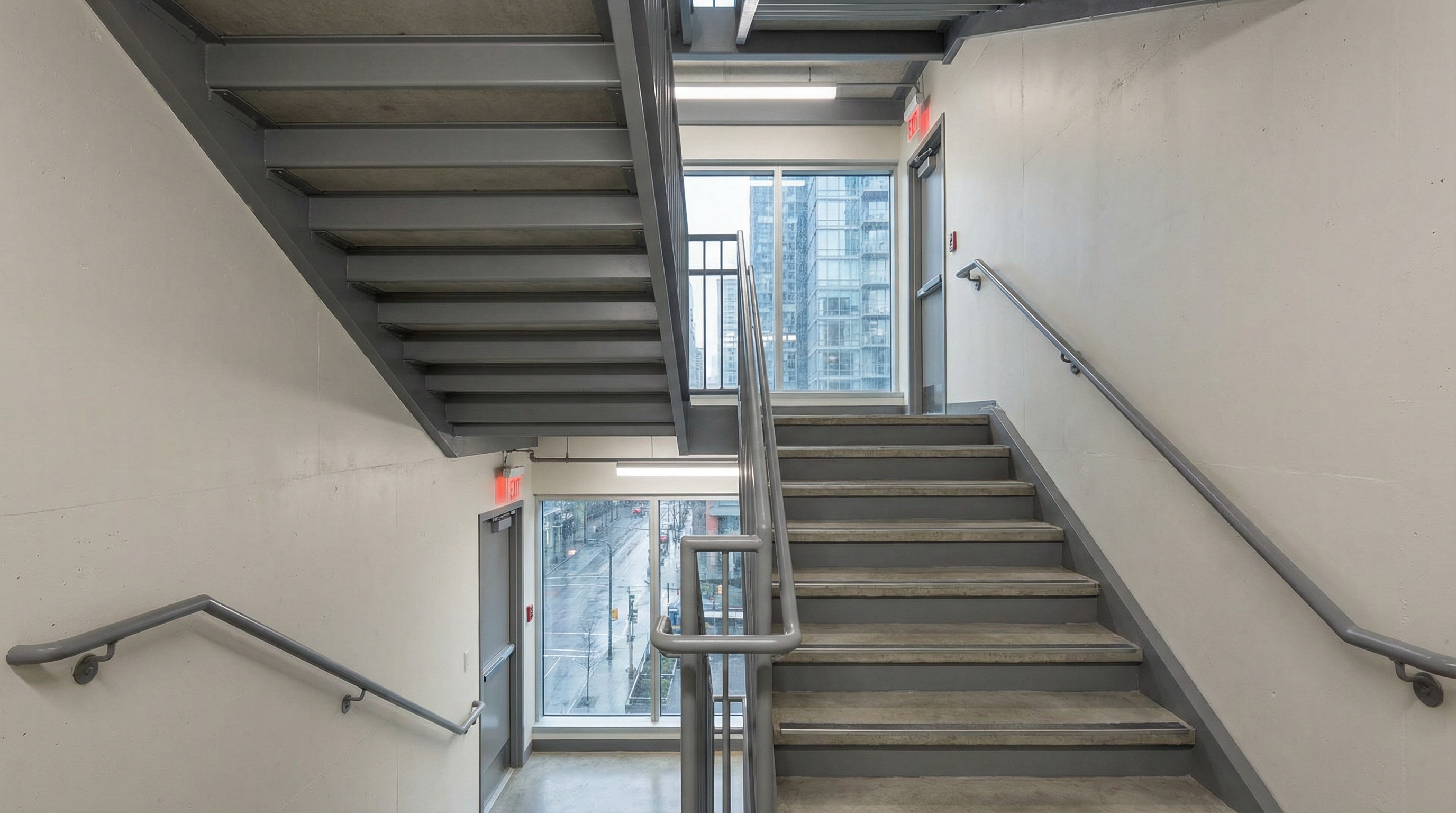 Commercial egress stair system in a modern Vancouver office building with painted steel stringers, concrete-filled metal pan treads, and hollow steel handrails, fabricated by Jeff and Simon Ironworks