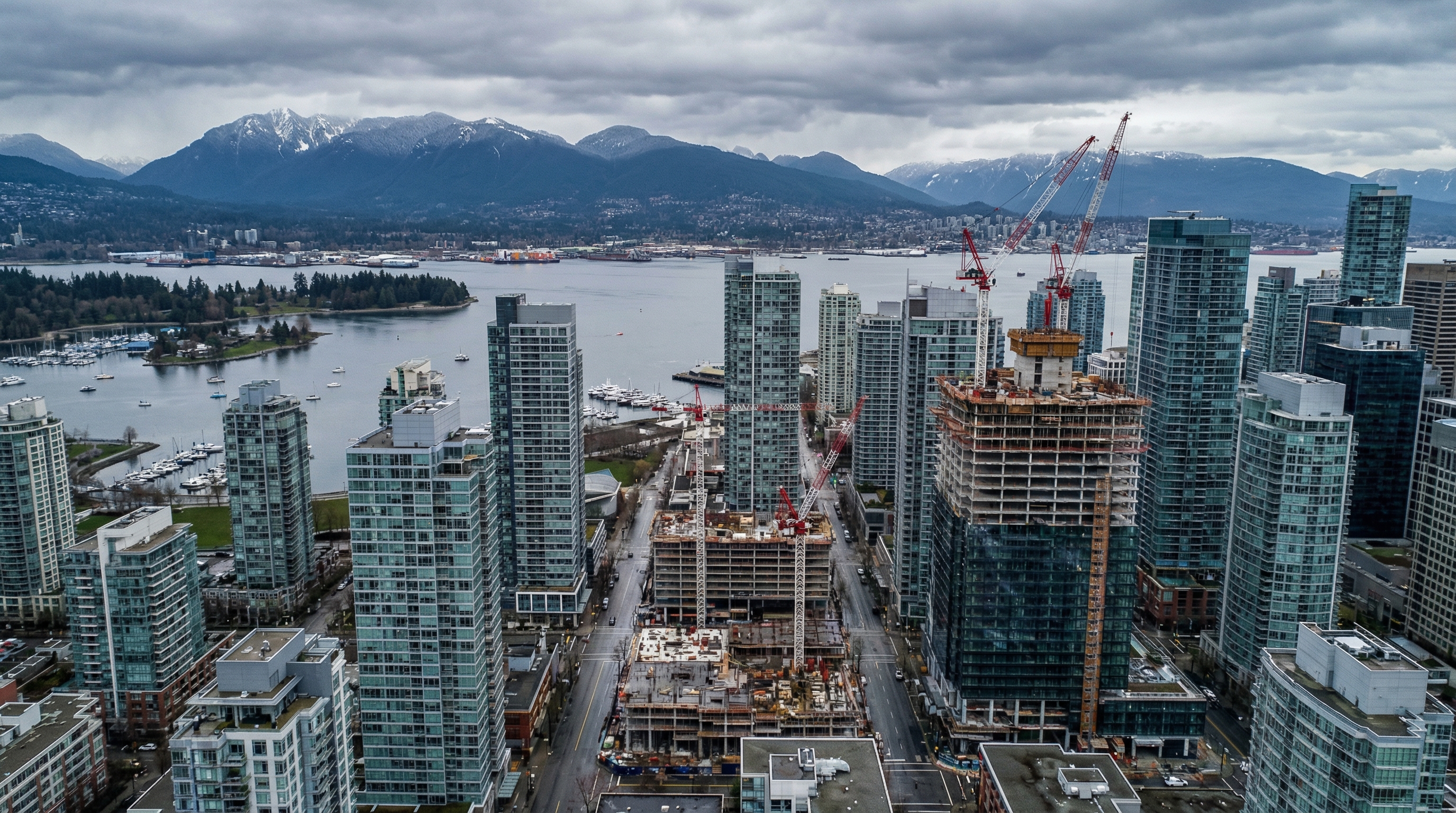 Aerial view of downtown Vancouver BC skyline with cranes and construction of modern glass towers, Burrard Inlet and North Shore mountains in background